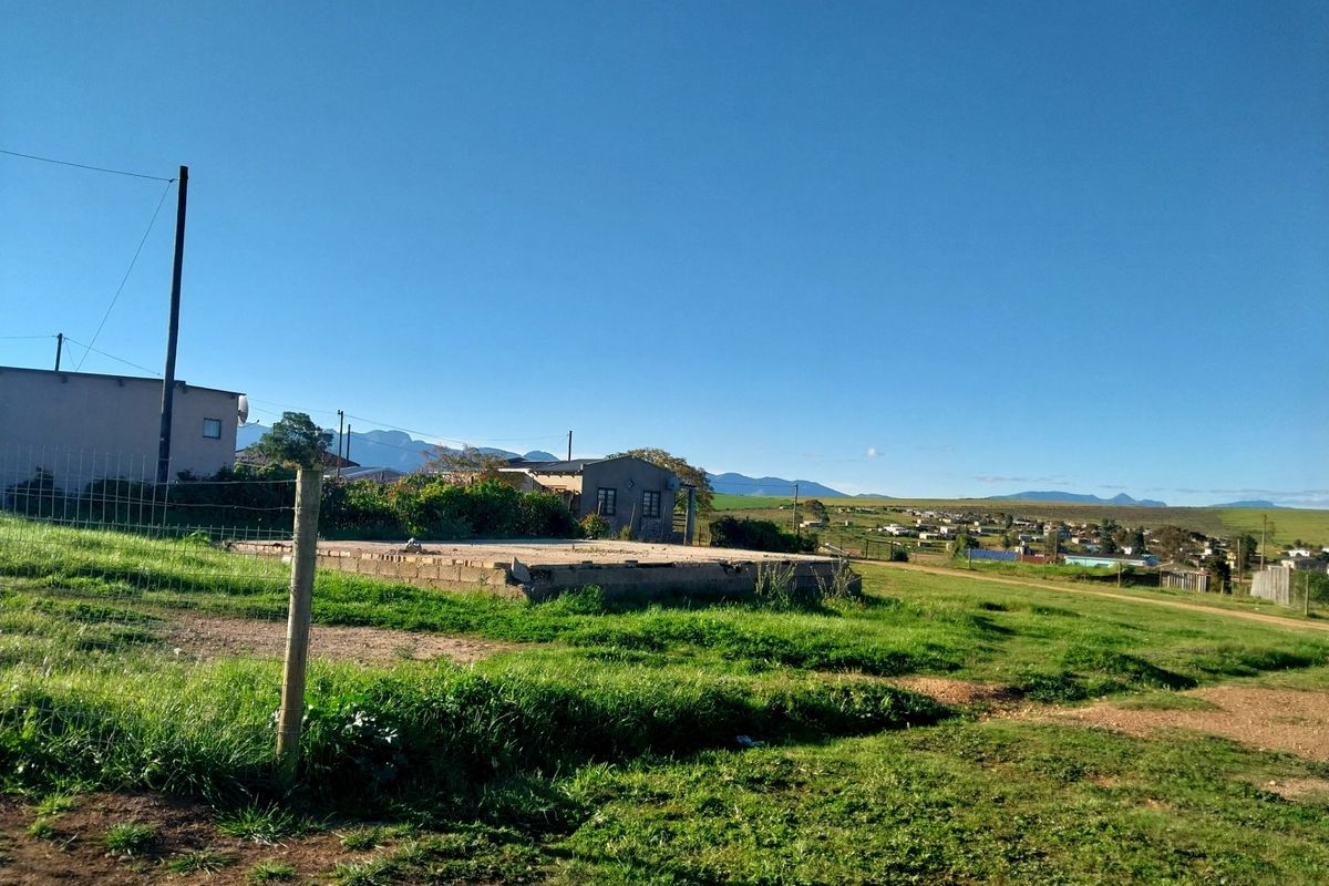 A vacant residential plot featuring an existing concrete foundation slab, wire fencing, and surrounding landscape with distant mountain views.