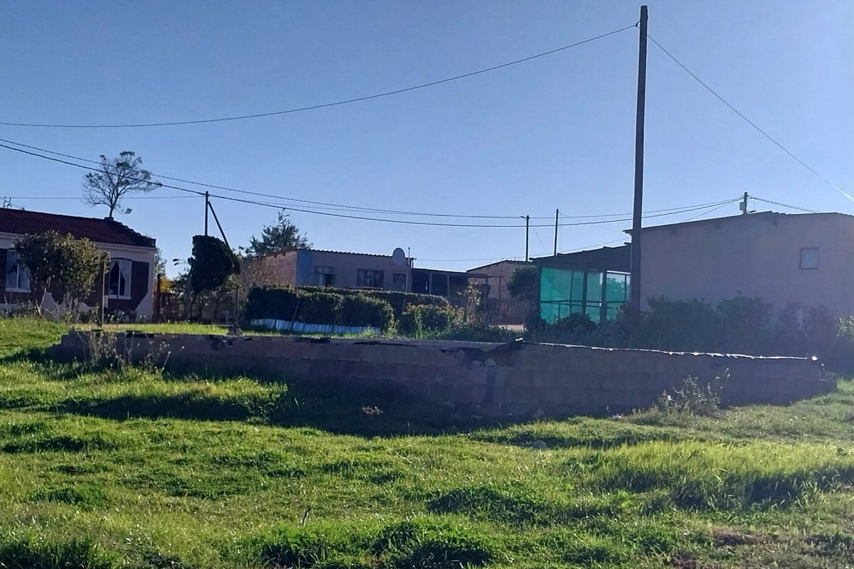 A vacant residential plot featuring an exposed concrete foundation and utility connections, situated in a neighborhood setting.