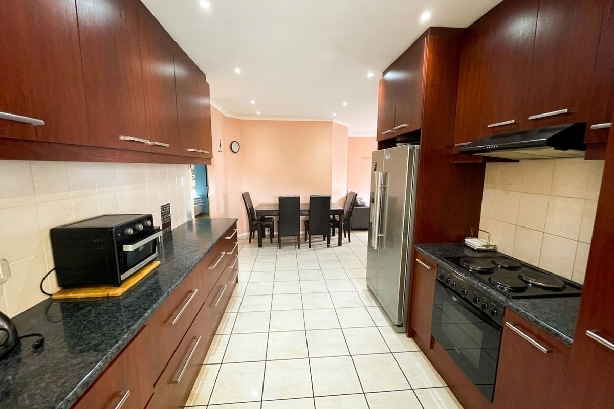 A functional galley-style kitchen featuring dark wood cabinetry, granite countertops, integrated appliances, and tiled flooring, leading into an adjacent dining area.