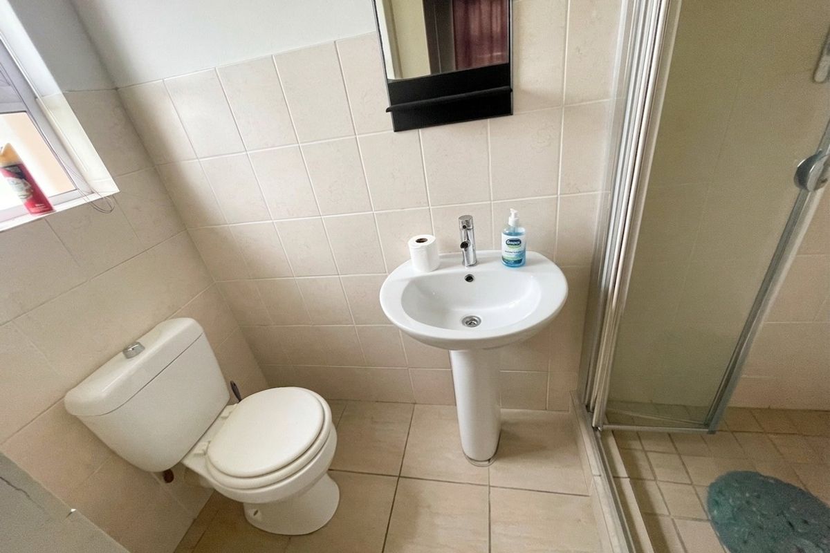 A functional bathroom featuring a pedestal basin, toilet, and a glass-enclosed shower with neutral ceramic wall and floor tiling.