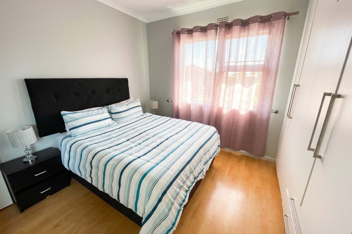 A well-maintained bedroom featuring light laminate flooring, neutral wall tones, and a built-in wardrobe for efficient storage.
