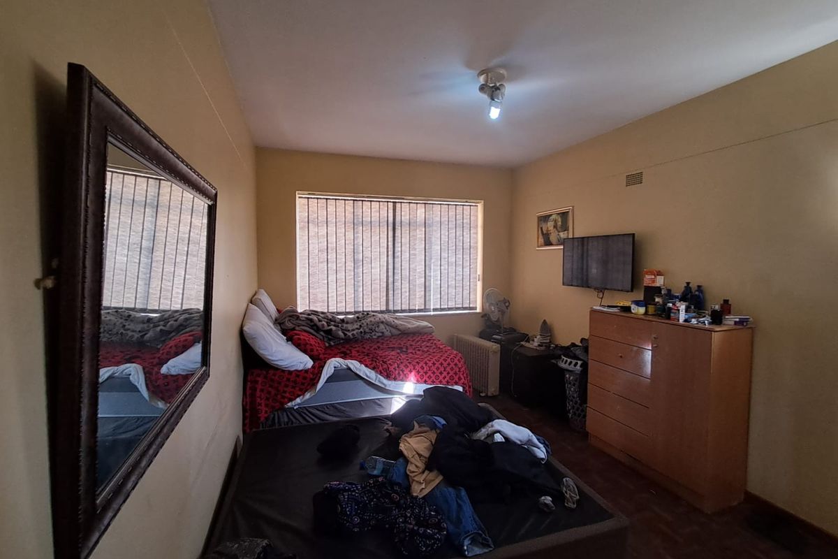 A bedroom featuring parquet flooring and vertical blinds, providing a functional space with natural light.