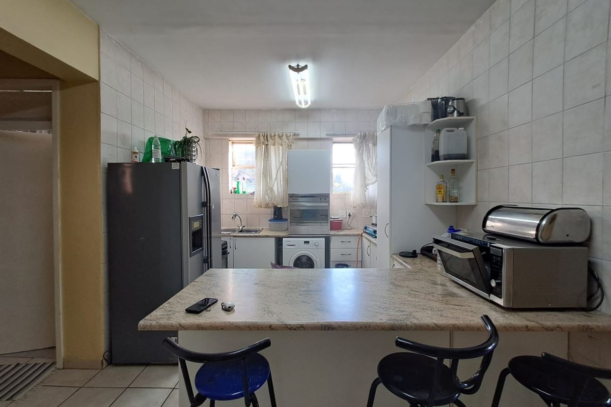 Functional kitchen featuring built-in cabinetry, laminate countertops, tiled backsplash, and integrated sink, offering a practical layout with potential for modern cosmetic updates.