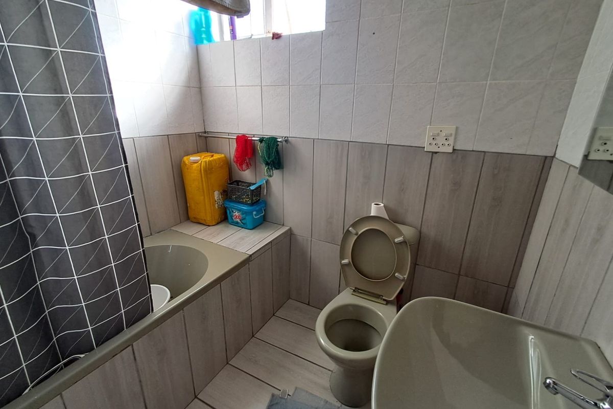 A compact bathroom featuring a built-in bathtub, toilet, and washbasin with neutral wall and floor tiling.