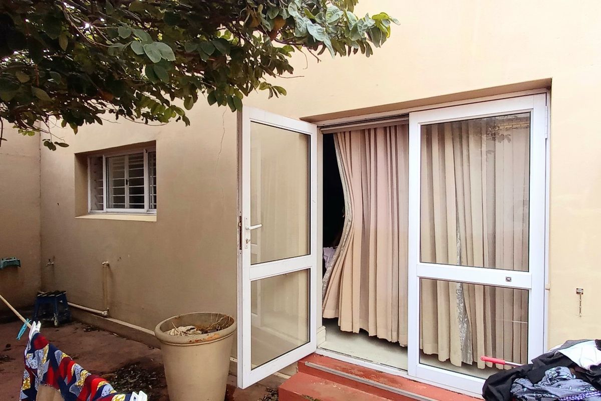 Rear exterior view of the property featuring a concrete patio area, uPVC framed sliding doors, and casement windows with security bars.