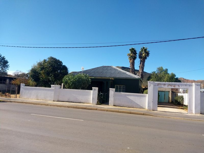 Front view of a residential property featuring a corrugated metal roof, perimeter boundary wall, and gated driveway access from the street.