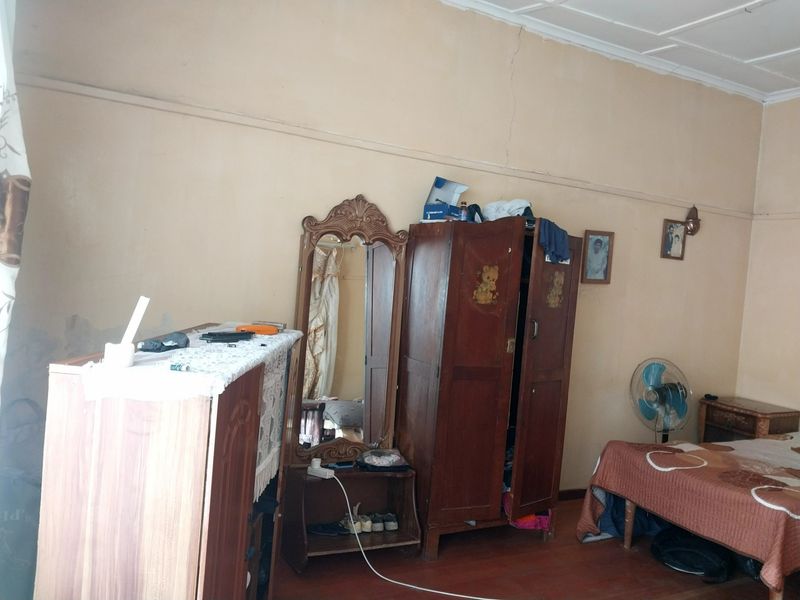 A bedroom featuring timber flooring and coved ceilings, currently showing signs of wear including wall cracks and paint deterioration.