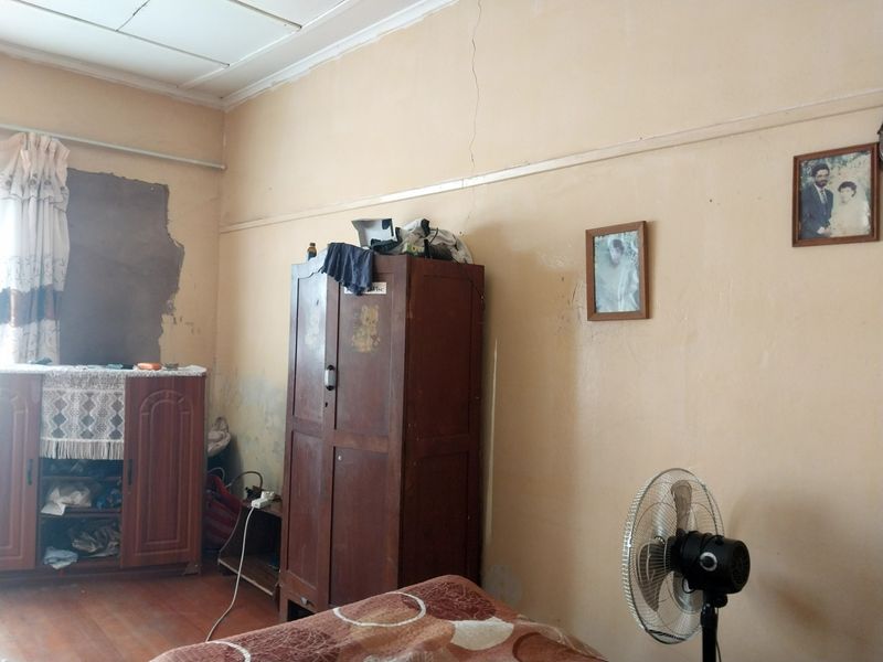 A bedroom featuring timber flooring and a picture rail, currently showing significant wall cracking and damaged plaster finishes requiring repair.
