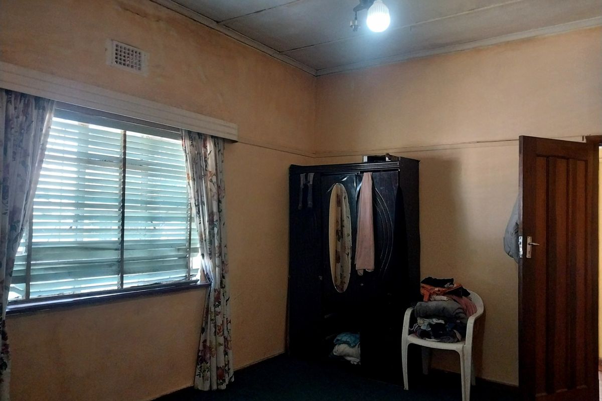A bedroom featuring a timber door, ventilation grille, and a window with venetian blinds, requiring cosmetic updates to the walls and ceiling.