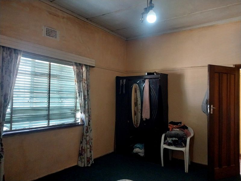 A bedroom featuring a timber door, ventilation grille, and a window with venetian blinds, requiring cosmetic updates to the walls and ceiling.