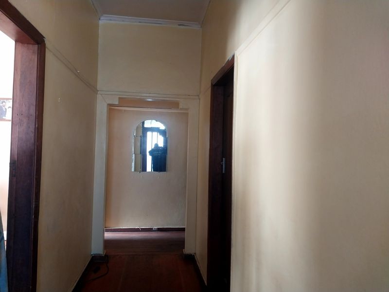 A narrow interior hallway featuring wooden door frames, an arched transition, and traditional wooden flooring, requiring cosmetic updates to improve its overall aesthetic.