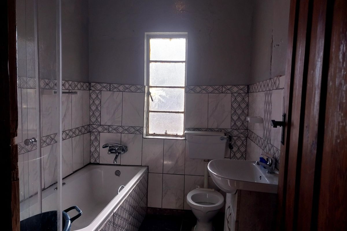 A functional bathroom featuring a bathtub, pedestal basin, and toilet with tiled finishes, requiring cosmetic updates to the walls and ceiling.