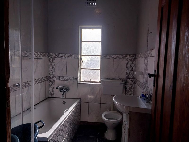 A functional bathroom featuring a bathtub, pedestal basin, and toilet with tiled finishes, requiring cosmetic updates to the walls and ceiling.