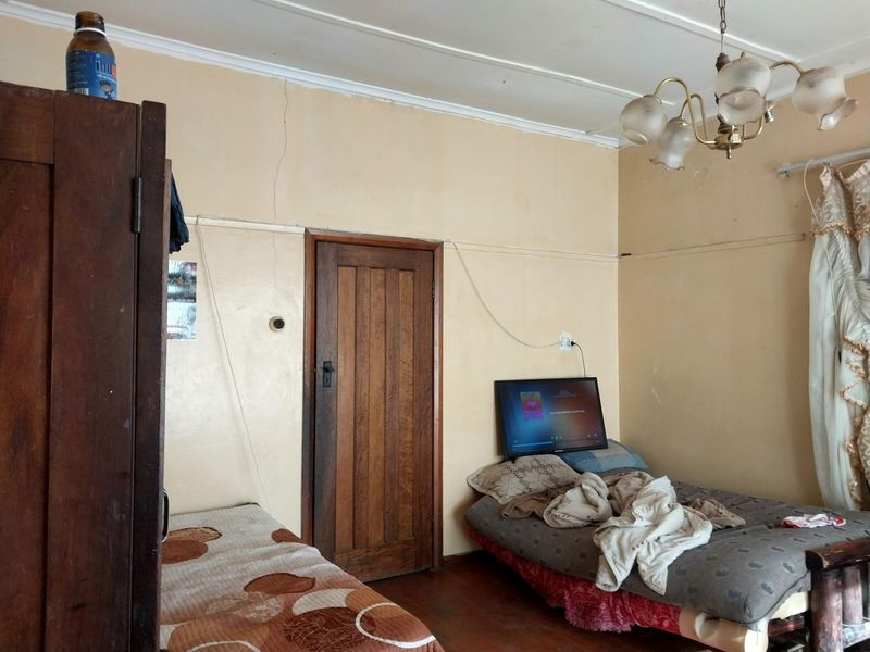 A bedroom featuring timber flooring, a classic chandelier, and a solid timber door, currently requiring maintenance and cosmetic updates to the wall finishes.