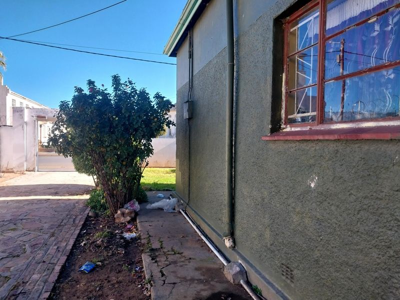 Side exterior view of the property showing a paved walkway, textured wall finish, and metal security bars on the window.