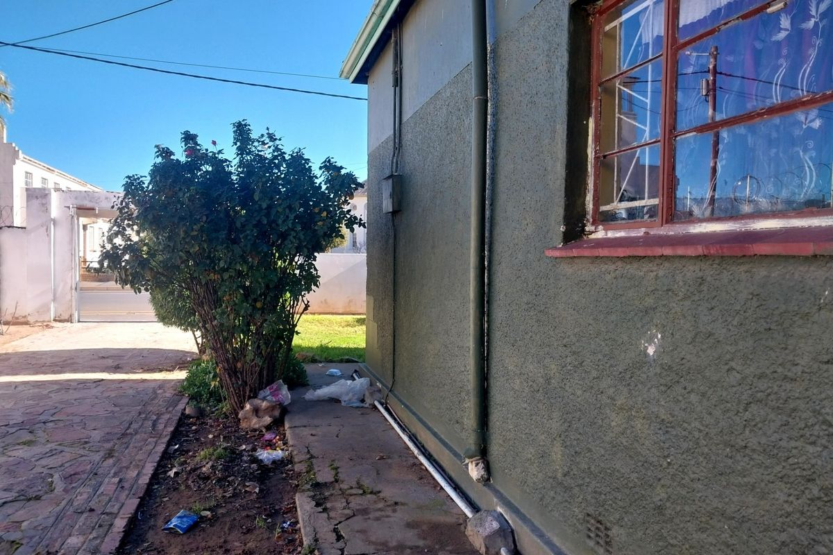 Side exterior view of the property showing a paved walkway, textured wall finish, and metal security bars on the window.