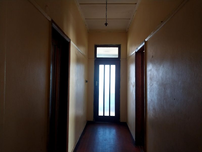 A narrow interior hallway featuring timber flooring, traditional door frames, and a transom window above the rear exit door.