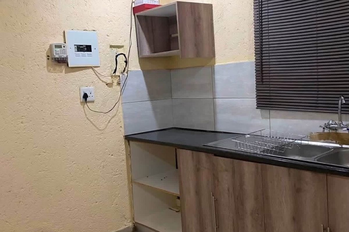 A compact kitchen area featuring laminate cabinetry, a stainless steel sink, and tiled flooring, currently requiring minor repairs and cosmetic updates.