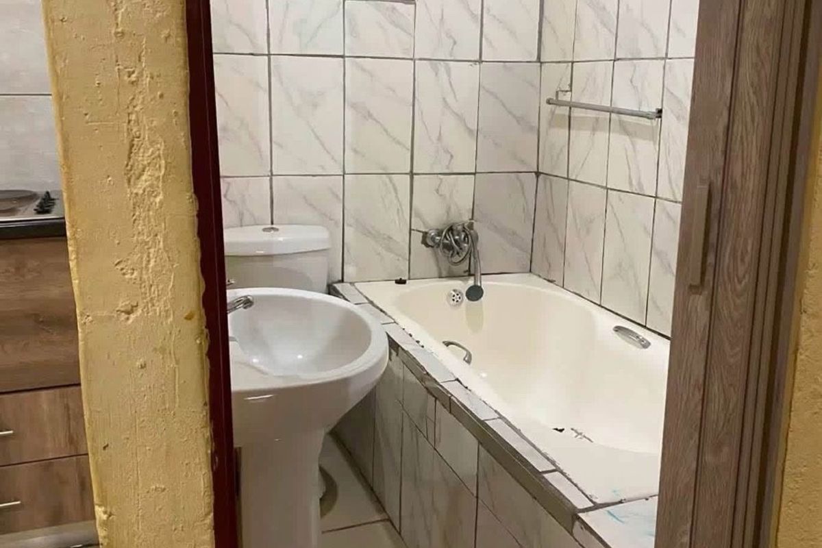 A compact bathroom featuring a pedestal basin, toilet, and bathtub with marble-effect wall tiling.
