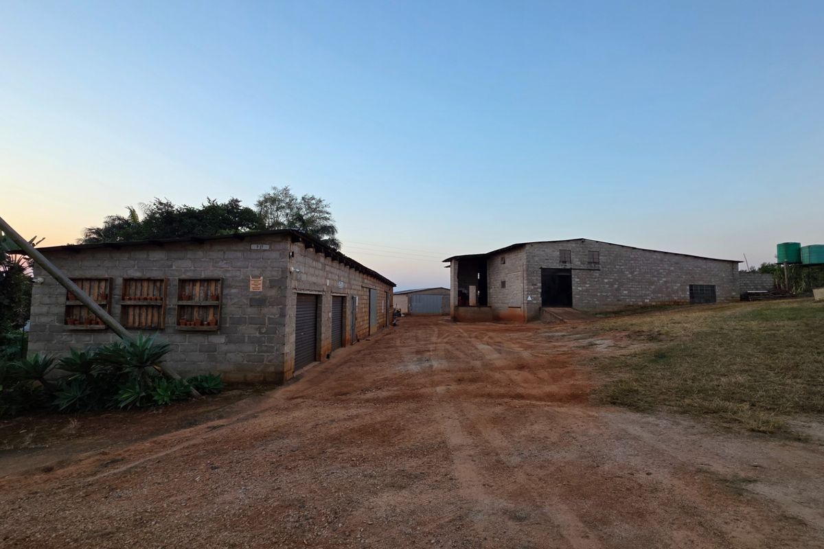 View of farm outbuildings featuring concrete block construction, metal roller doors, and corrugated roofing situated along a dirt access path.