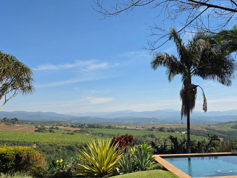 Scenic elevated view overlooking expansive agricultural farmland and rolling hills, featuring a private swimming pool and established garden landscaping.