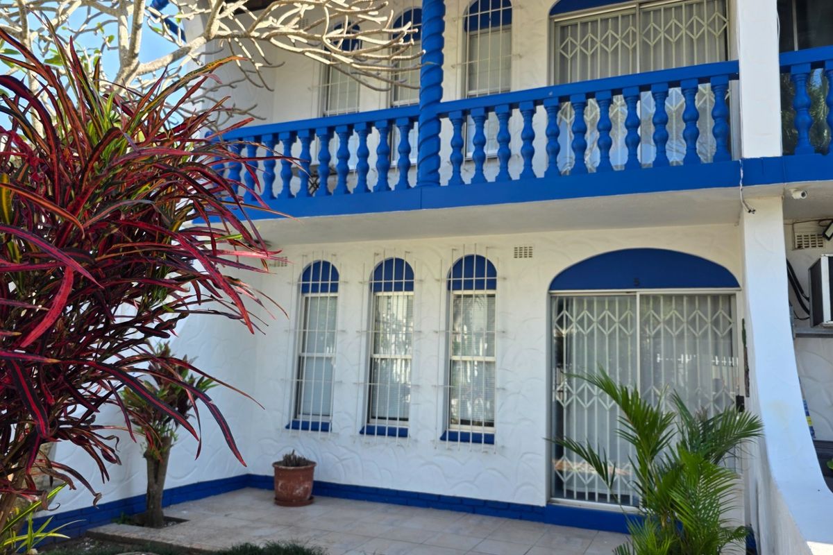 Rear exterior view of a two-story townhouse featuring a tiled patio, upper balcony with blue balustrades, and security bars on windows and doors.
