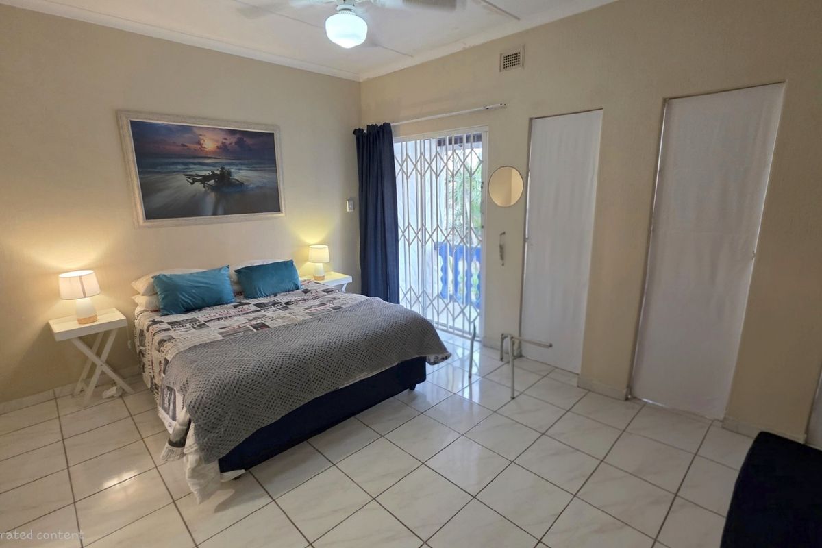 A bedroom featuring tiled flooring, built-in cupboards, and a sliding glass door with a security gate providing access to the exterior.