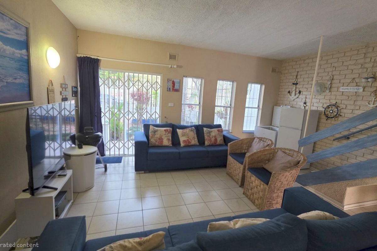 A living room featuring tiled floors, an exposed brick feature wall, and access to an outdoor area through a sliding glass door with security gate.