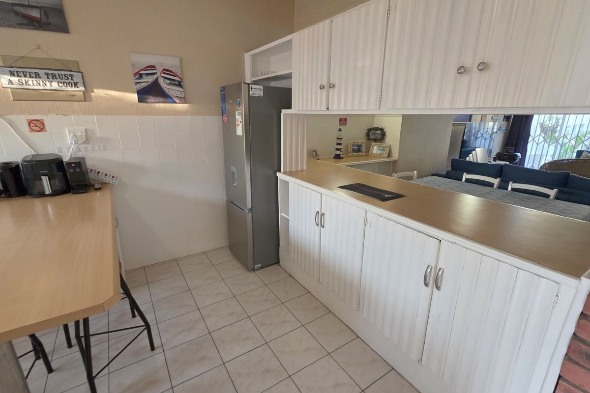 A functional kitchen area featuring white built-in cabinetry, laminate countertops, tiled flooring, and a tiled splashback, with an open-plan layout connecting to the living space.