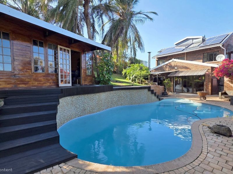 Outdoor pool area featuring a swimming pool, timber decking, mosaic tiling, and brick paving, set against a timber cabin and main brick residence.