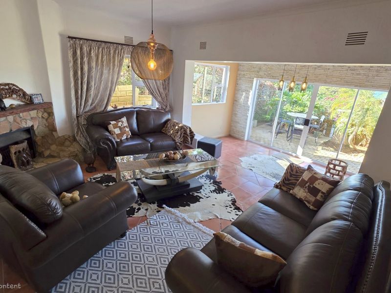 Spacious living room featuring a stone-clad fireplace, terracotta flooring, and large sliding glass doors that open to a private patio area.