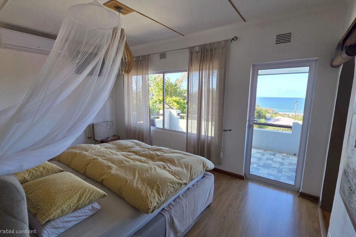 A bright bedroom featuring laminate flooring, a split-system air conditioner, and direct access to a private balcony with scenic ocean views.
