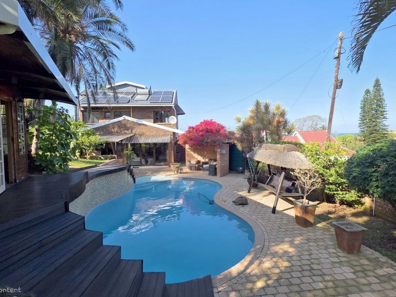 A well-maintained outdoor pool area featuring timber decking, paved patio space, and a view of the main residence with solar panels installed.