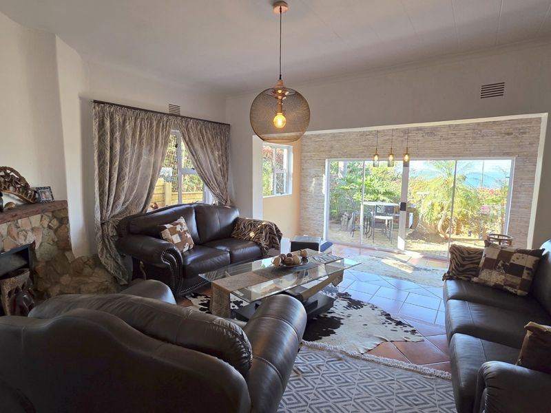 Spacious living room featuring a stone fireplace, tiled flooring, and large sliding glass doors that open to a garden patio area.