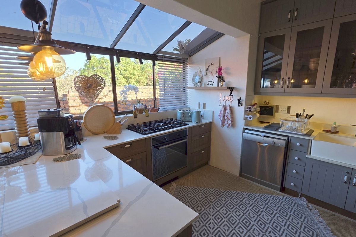 A bright, modern kitchen featuring shaker-style cabinetry, quartz countertops, a farmhouse sink, and a unique glass-roof conservatory design.