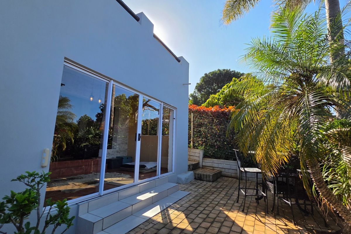 Rear exterior view featuring a paved patio area with sliding glass door access to the home and landscaped garden surroundings.