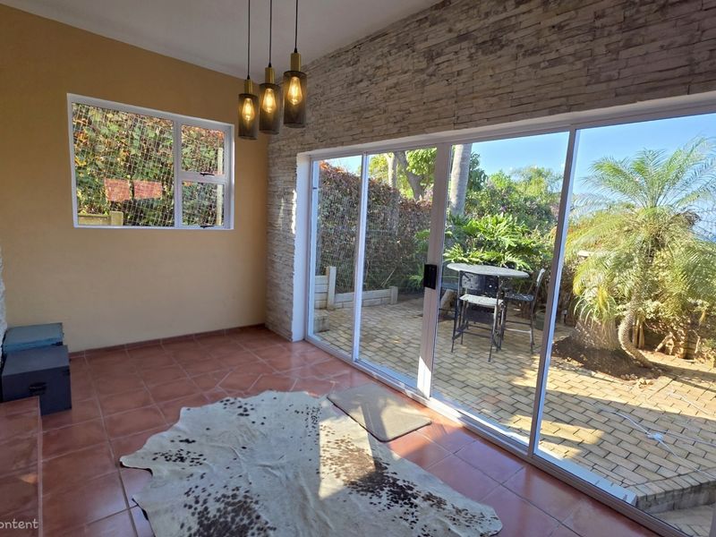Bright living area featuring terracotta flooring, a stone veneer accent wall, and large sliding glass doors providing seamless access to the outdoor patio.