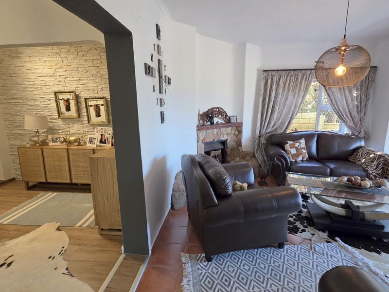 A living room featuring a stone fireplace, mixed flooring types, and an open-plan layout connecting to an adjacent space.