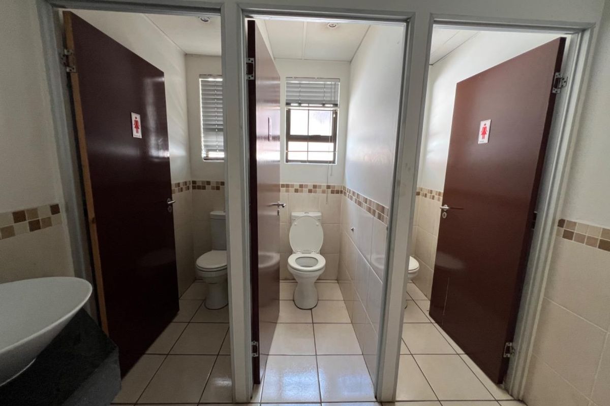 Commercial restroom facility featuring three individual toilet cubicles with privacy doors and a shared vanity area with tiled finishes.