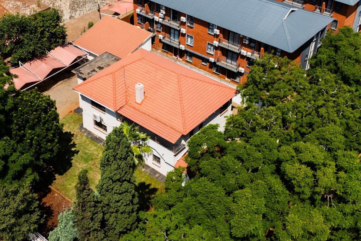 Aerial view of the commercial property featuring a terracotta tiled roof, established garden surroundings, and adjacent multi-story building infrastructure.