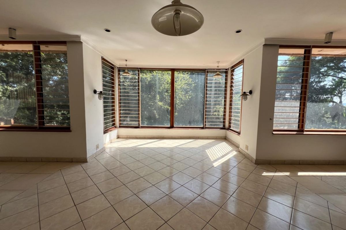 A bright, empty living area featuring large louver windows, tiled flooring, and a combination of recessed and wall-mounted lighting.