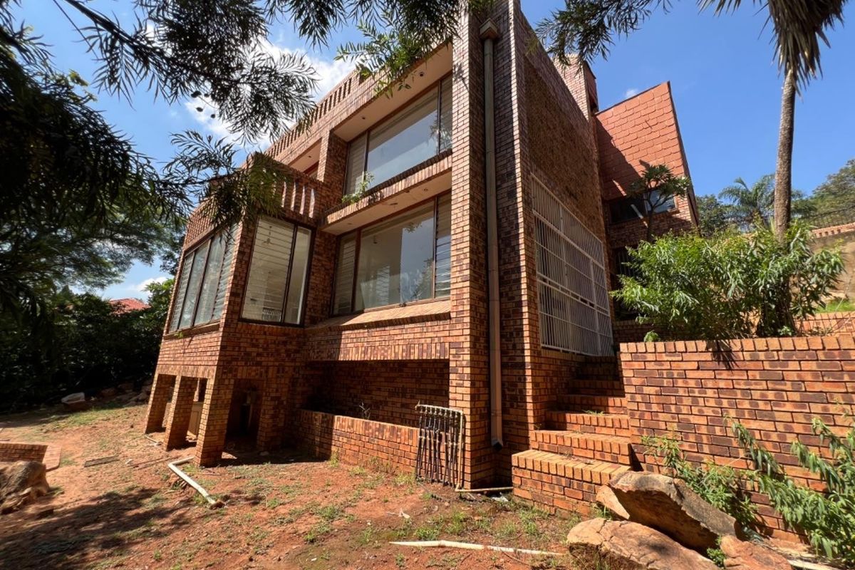 Rear view of a multi-story face brick house featuring large windows, brick retaining walls, and an expansive garden area.