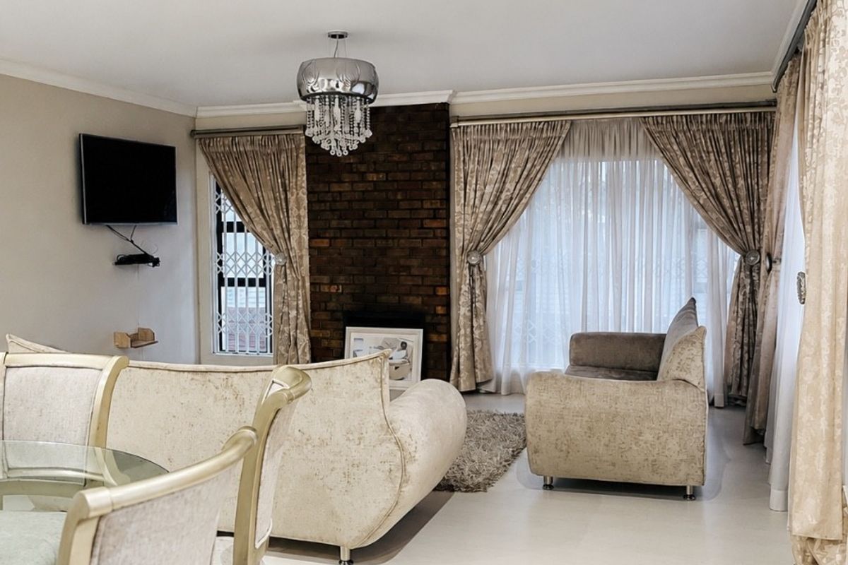 A well-maintained living room featuring an exposed brick fireplace, tiled flooring, and recessed lighting, creating a comfortable and inviting atmosphere.