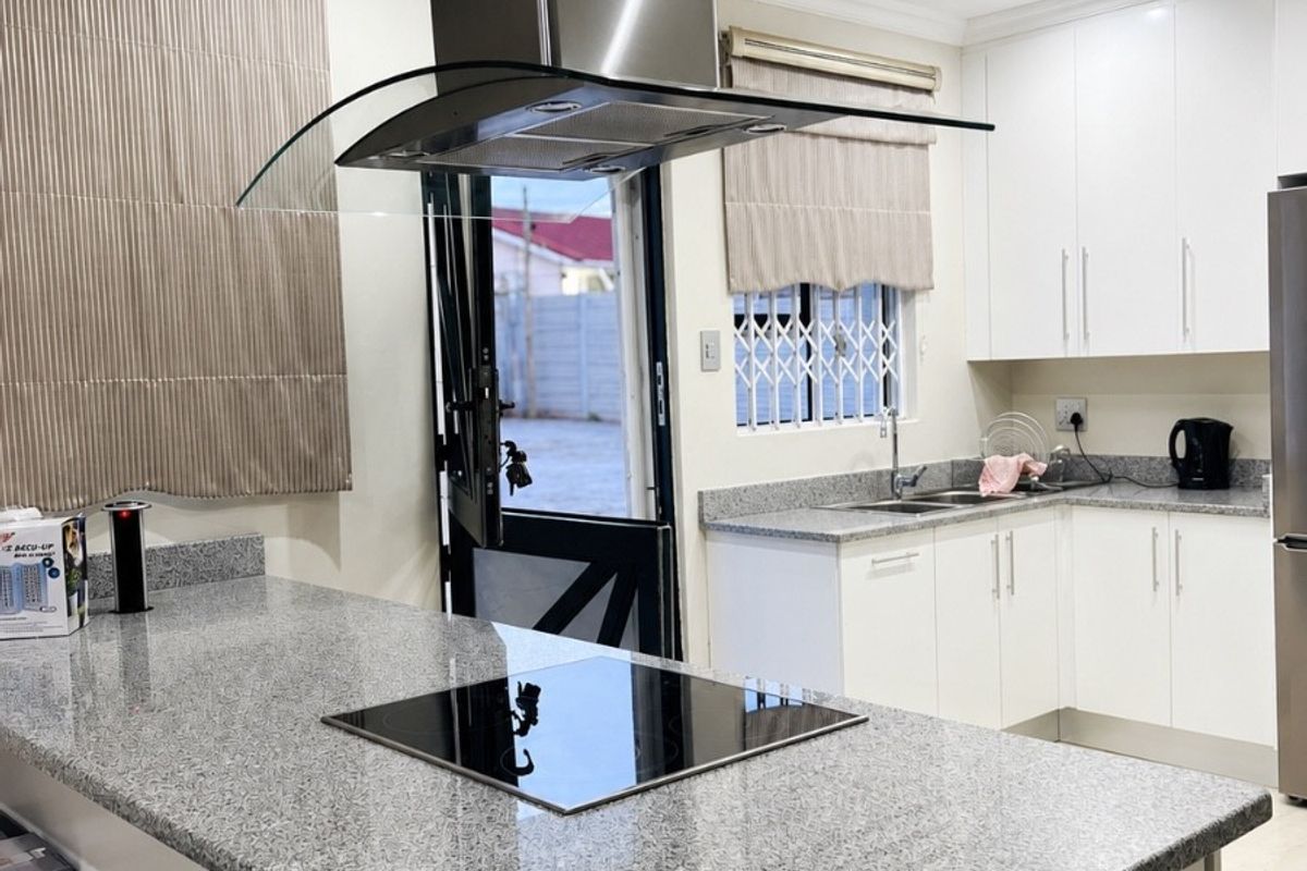 Modern kitchen featuring granite countertops, built-in cabinetry, a central island with an integrated electric hob, and a stainless steel extractor fan.