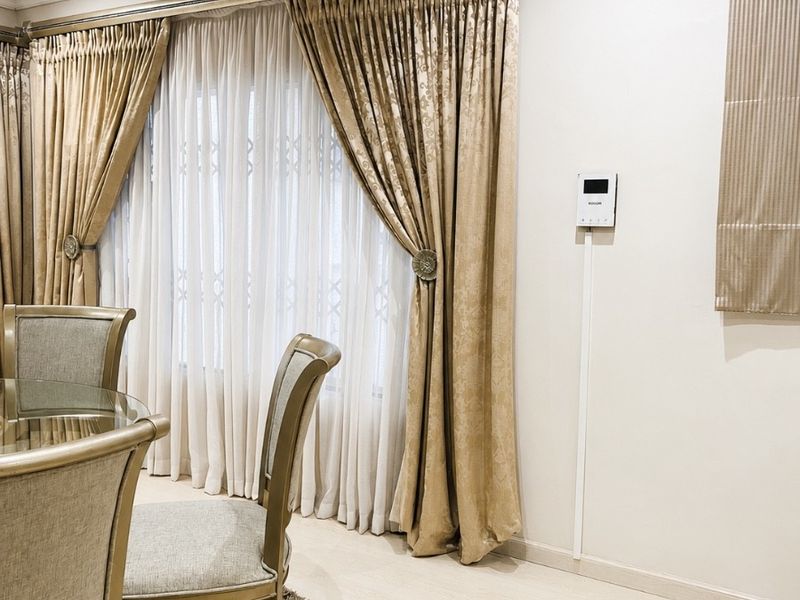 A well-maintained dining area featuring neutral laminate flooring, recessed ceiling lighting, and an integrated intercom system with elegant floor-to-ceiling curtain treatments.