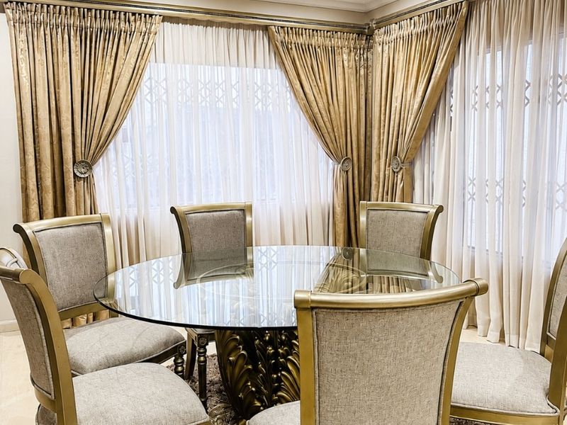 A well-lit dining room featuring large windows with elegant floor-to-ceiling curtains and integrated security gates, creating a formal and inviting atmosphere.