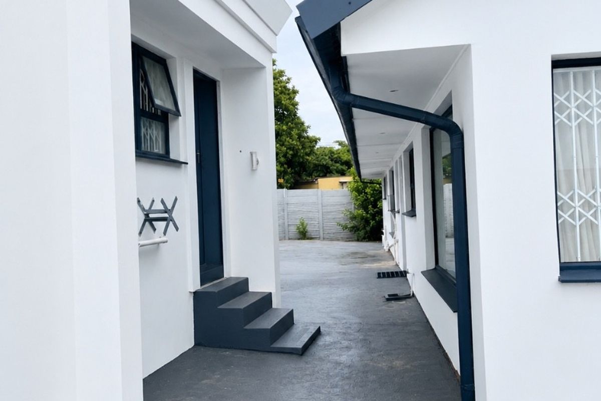 A clean exterior view of the guest house rear pathway, featuring modern white facades, dark trim, and paved access between building sections.