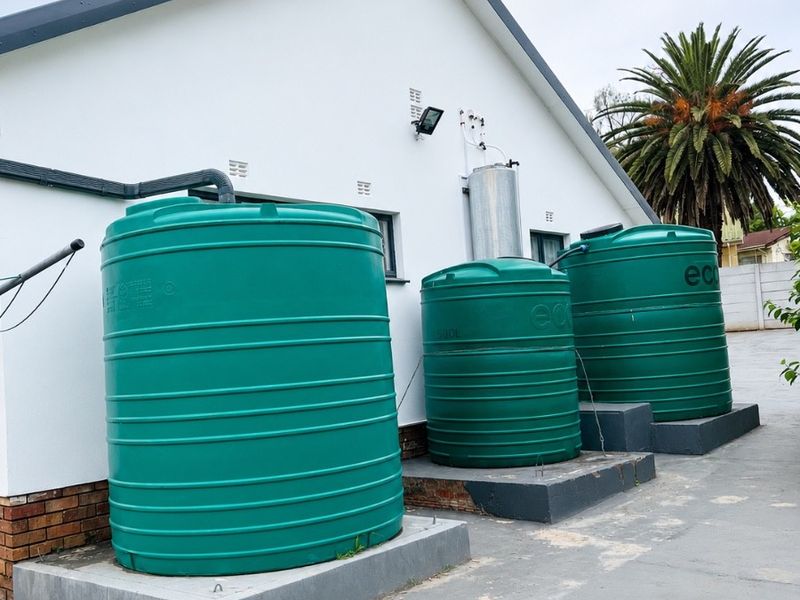 Rear exterior view of the property featuring a series of green water storage tanks mounted on concrete plinths with associated plumbing infrastructure.