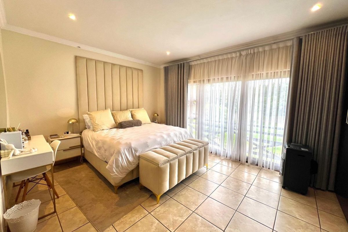 Spacious bedroom featuring neutral tiled flooring, recessed lighting, and large sliding glass doors with floor-to-ceiling curtains providing ample natural light.