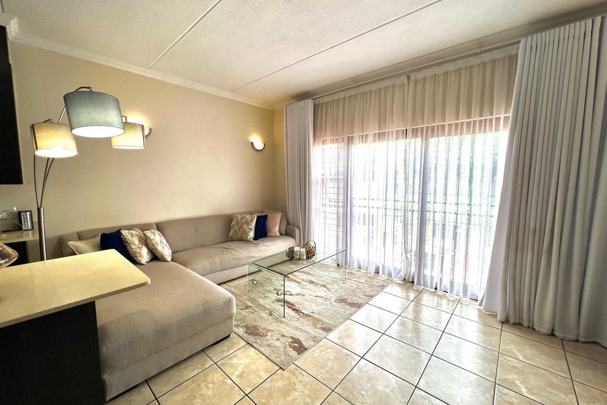 A bright living room featuring tiled flooring and large sliding glass doors with floor-to-ceiling curtains, providing ample natural light and access to the exterior.